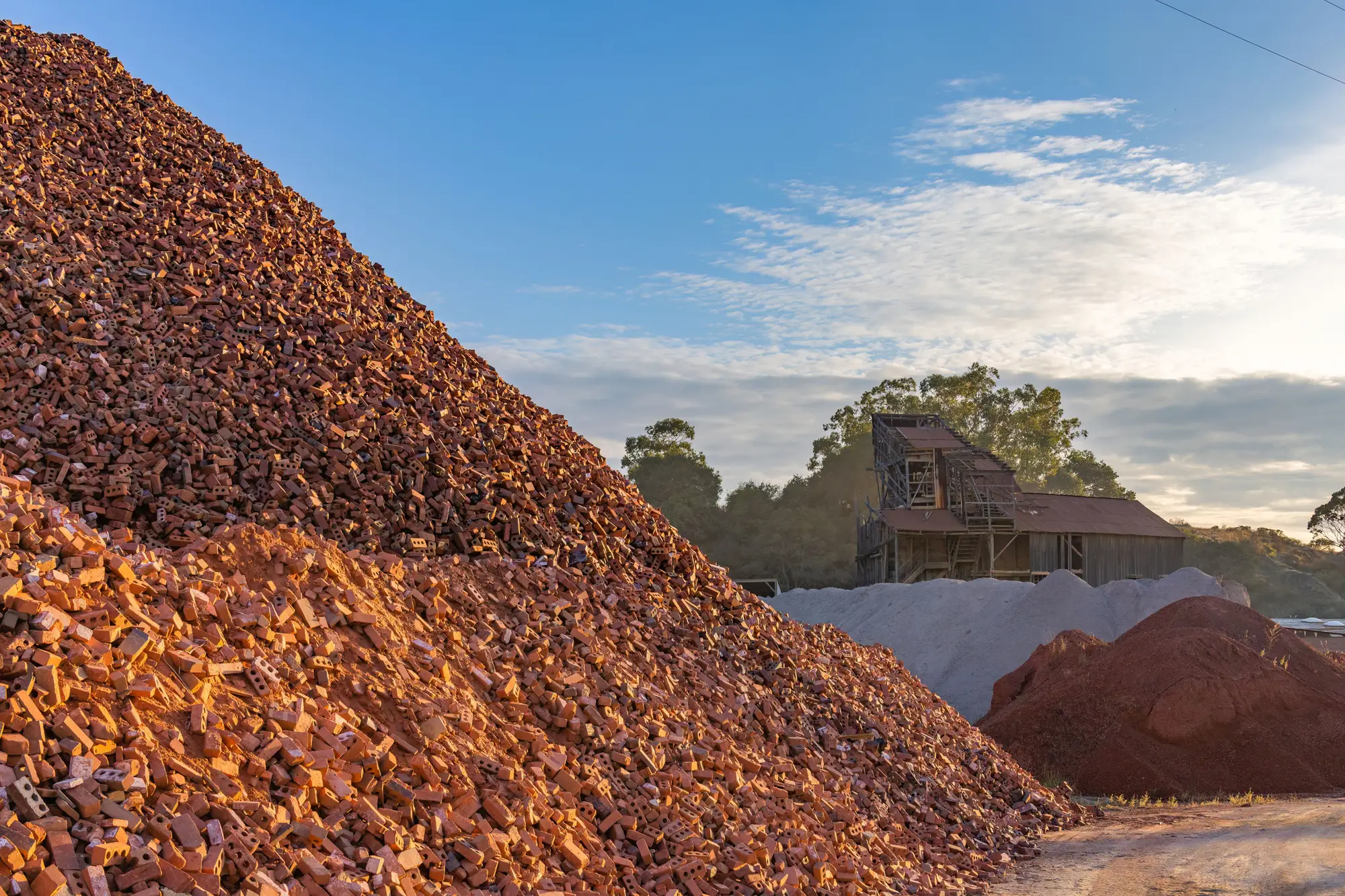 Piles of crushed brick and sand at a materials yard under a clear sky